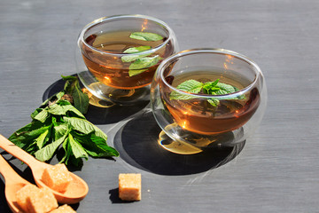 Alternative tea with mint, lemon, brown sugar in two glasses of tea with wooden spoons on a gray background. Healthcare tea, alternative medcine