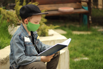 A child in a medical mask is reading a book in the street.