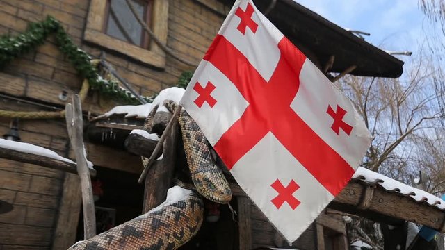Flag of Georgia country waving in the wind in winter time. Georgian flag on the flagpole waving in the background of a restaurant in georgian skiing resorts