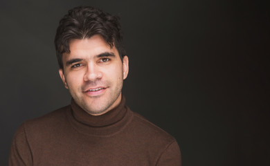 a young dark man in a turtleneck is smiling against a dark background