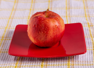 A red Apple on a red plate on the table. Drops of water glisten on the Apple.