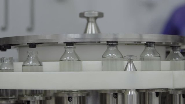 glass bottles filled and sealed with rubber caps on a medical solution conveyor line close up medical industry