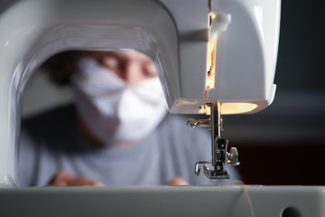 Woman works with sewing machine from home, wearing protective mask during the quarantine period caused by coranavirus.