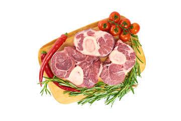 Three slices of fresh shank steak, with a sprig of rosemary, red pepper, and cherry tomatoes are on the cutting board on a white background. Fresh Osso Bucco steaks. The view from the top.