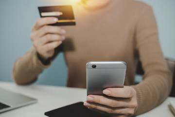 young woman entering security code with mobile phone and paying with mock up credit card and laptop computer on desk at home office, shopping online, electronic pay and digital technology concept
