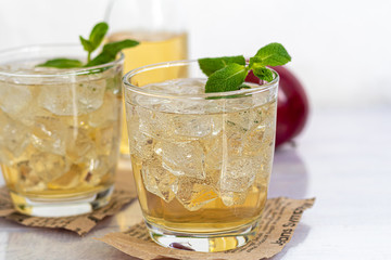 Healthy organic foods. Apple cider in a glass bowl and fresh red apples on a light background. In a glass of ice cubes and nearby cinnamon sticks.