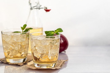 Healthy organic foods. Apple cider in a glass bowl and fresh red apples on a light background. In a glass of ice cubes and nearby cinnamon sticks.