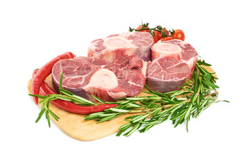 Three slices of fresh shank steak, with a sprig of rosemary, red pepper, and cherry tomatoes are on the cutting board on a white background. Fresh Osso Bucco steaks.