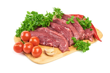 Slicing fresh meat steaks, with young basil, red pepper, garlic and cherry tomatoes on a cutting board on a white background. Fresh flank steak. The view from the top.