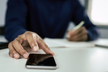 Fototapeta premium businessman in blue shirt hand working on digital mobile phone and writing about finance with document report on desk at home office, work from home, digital marketing and financial business concept