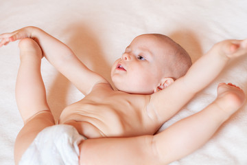 The baby is lying on his back on a white bed. He spread his legs like a circus performer. Laughter, children's joy and fun. Products for children, changing diapers. The care for the baby.