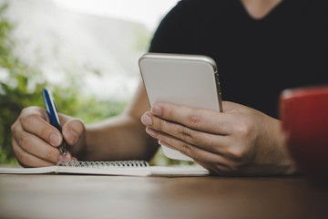 man relaxed writing and working with digital mobile smart phone, report document with red coffee cup on desk at cafe restaurant, work from home, digital technology, internet, online business concept