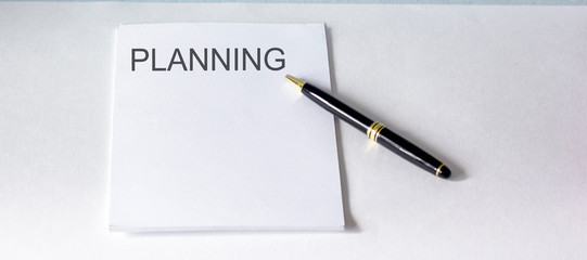 White notebook with planning text on a white background with pen
