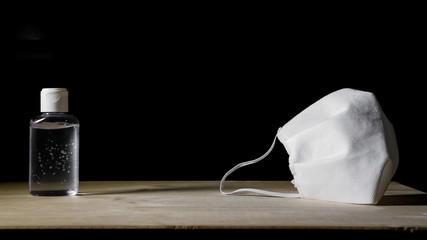 Coronavirus prevention - hand sanitizing gel and protective mask on wooden table with black background