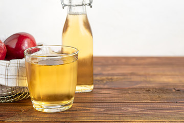 Healthy organic foods. Apple cider in a glass bowl and fresh red apples on a wooden background. In a glass of ice cubes and nearby cinnamon sticks.