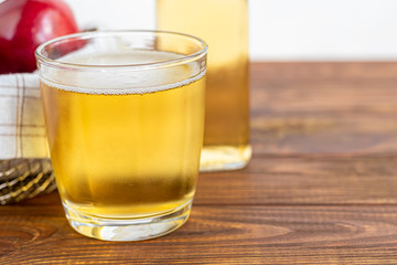Healthy organic foods. Apple cider in a glass bowl and fresh red apples on a wooden background. In a glass of ice cubes and nearby cinnamon sticks.