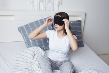 Young woman woke up in the morning in bed and takes off the sleep mask, good morning,