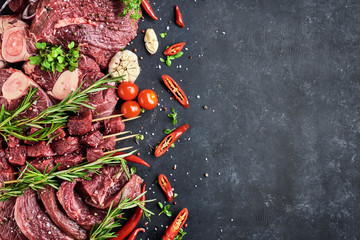 FreVarious fresh meat-portioned steaks, beef tenderloin, shin steaks, meat on skewers lie on a dark...