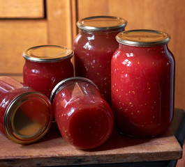 Preserving of tomato paste or juice, homemade vitamin drink in glass jars on wooden board, closeup, copy space, vertical, homegrown healthy food concept