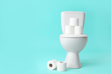 Toilet bowl with rolls of paper on color background