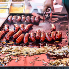 Sausages are being grilled on a large hot plate along with chopped onions.