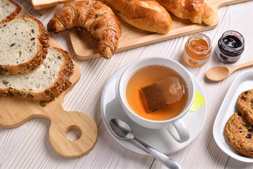 Top view of cup of tea with breads or bun, croissant and bakery on white wooden table