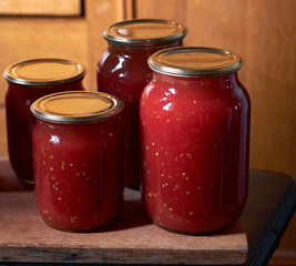 Preserving of tomato paste or juice, homemade vitamin drink in glass jars on wooden board, closeup, copy space, vertical, homegrown healthy food concept