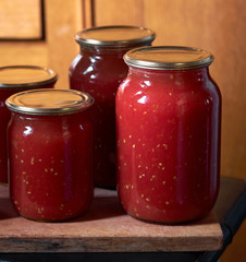 Preserving of tomato paste or juice, homemade vitamin drink in glass jars on wooden board, closeup, copy space, vertical, homegrown healthy food concept