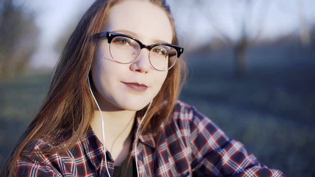 Teenager girl with long hair, light brown eyes and stylish glasses, smiles pretty 
and modestly in front of a camera. 
The wind gently moved her hair .Straightens hair  with hand .
