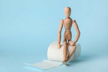 Toilet paper with wooden human figure on color background
