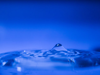Water drop creating waves ripples and air borne water droplet