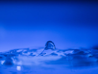 Water drop creating waves ripples and air borne water droplet