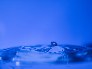 Water drop creating waves ripples and air borne water droplet