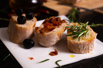 Sliced bread with olive oil, black olives, tomatoes and rosemary on a black background.  Mediterranean typical food.