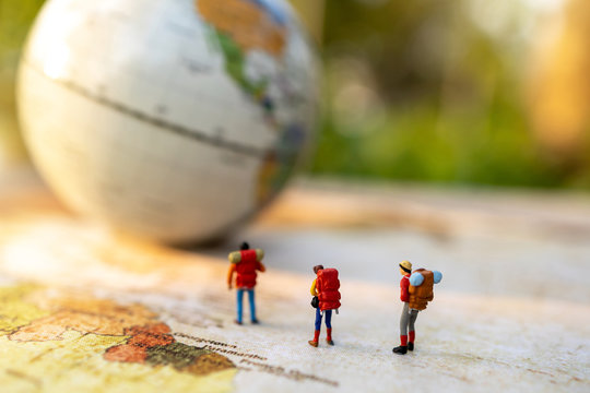 Minature people: traveling with a backpack standing on vintage world map and globe,  Travel and vacation concept.