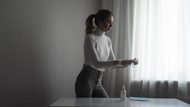 Pandemic Coronavirus Covid-19. A young woman wears a disposable facial medical mask and gloves to protect the spread of infection. Epidemic. Life in quarantine and self-isolation