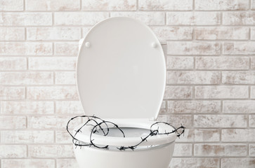 Toilet bowl with barbed wire on brick background. Hemorrhoids concept