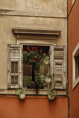Fototapeta na wymiar Ventana vieja con celosías gastadas, decorada con flores, en un edificio de Split, Croacia