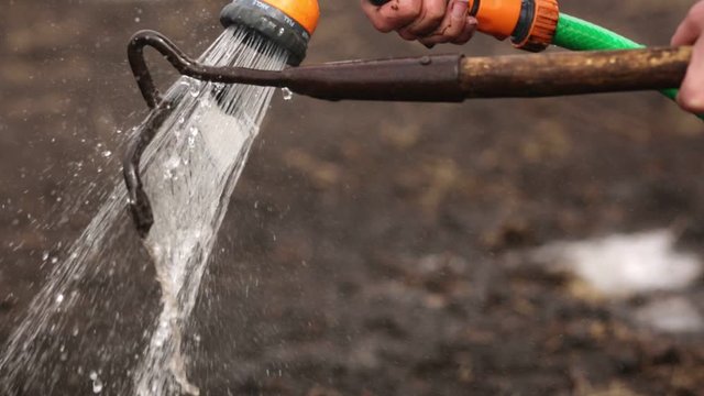 Professional worker washes glander with special washing tool, specialist cleaning instrument after working in garden, wash gardens after making holesfor seedings in ground. Agriculture working.