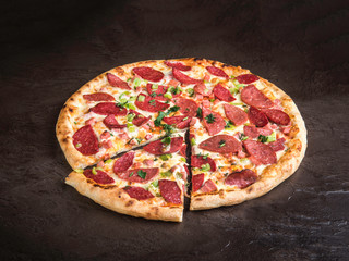 Delicious pizza with sausages, cheese and slices of bell pepper lies on a dark stone surface