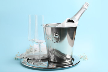 Bucket with ice, bottle of champagne and glasses on color background