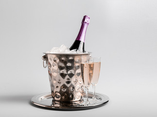 Bucket with ice, bottle of champagne and glasses on light background