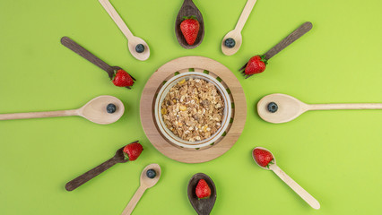 Bowl of muesli with with fresh strawberries and blueberries on solid green background. Healthy breakfast concept. Vege meals concept. 
