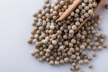 white peppercorns in wooden scoop on white background