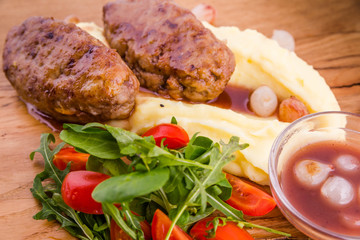 A dish of meat cutlets, mashed potatoes, fresh vegetables and sauce on a wooden board on a white background