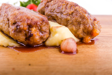 A dish of meat cutlets, mashed potatoes, fresh vegetables and sauce on a wooden board on a white background
