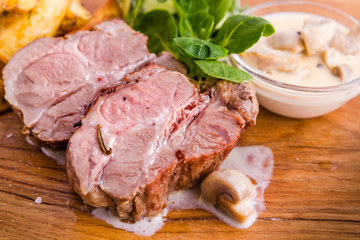 Fried pork neck with potato..gratin and creamy mushroom sauce on a wooden board