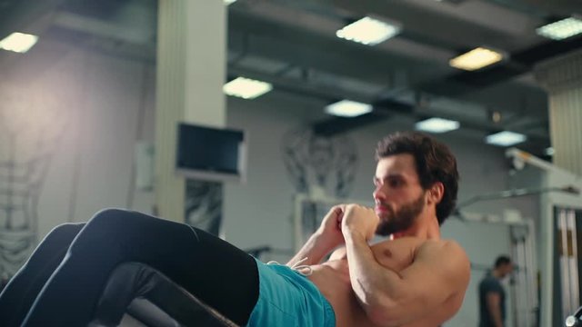 Sportive bearded young man with muscular wiry naked torso doing abs exercises during sport workout training in modern gym. Concept of healthy lifestyle. Shooting in slow motion.