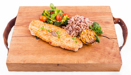 Golden grilled fish fillet with a side dish of rice and vegetables on a wooden board on a white background