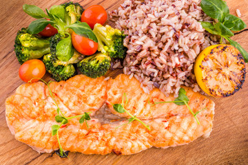 Golden grilled fish fillet with a side dish of rice and vegetables on a wooden board on a white background